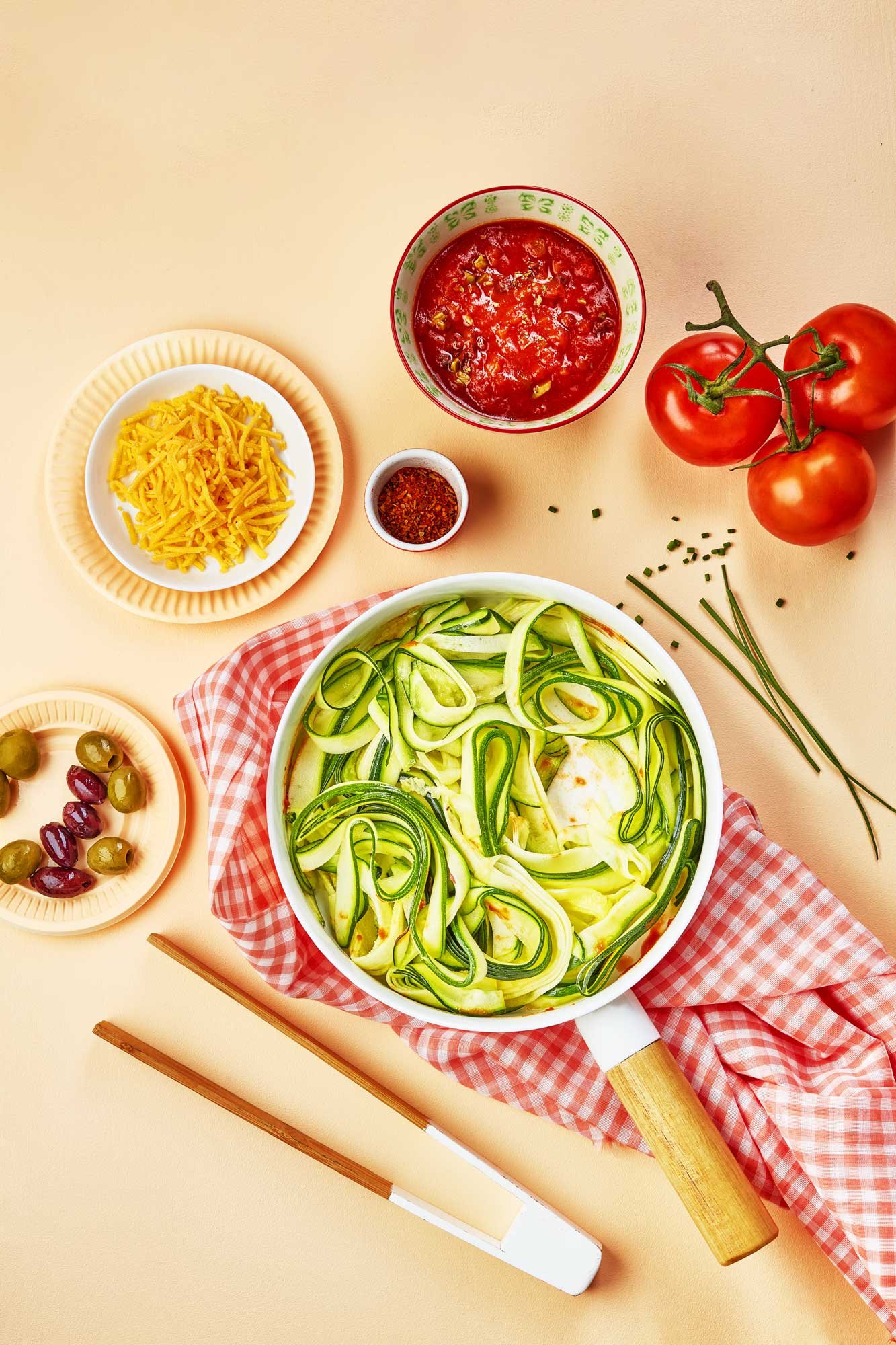 photographie culinaire en ambiance saumon clair, tagliatelles de courgettes, sauce tomate, cheddar râpé, olives