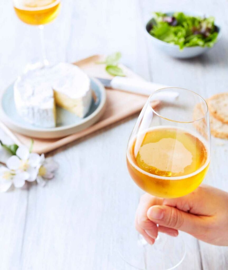 gros plan sur un beau verre de cidre, camembert et salade en arrière plan, pris par un photographe culinaire spécialisé boissons