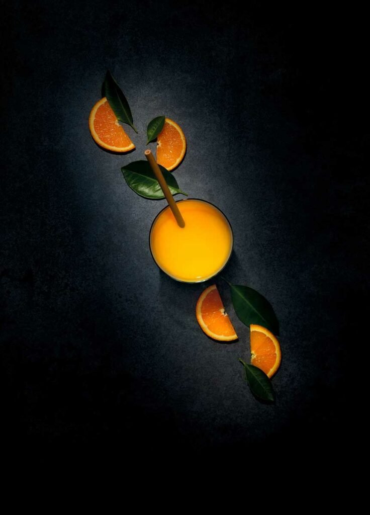 photographie alimentaire en clair obscur de jus d'orange avec tranches d'orange et feuilles d'oranger