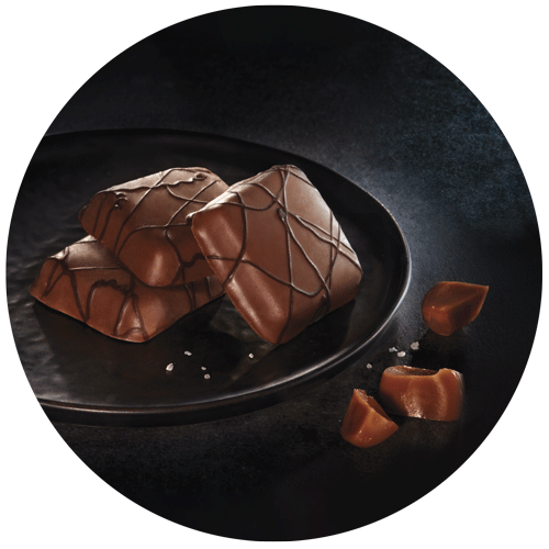 photographie culinaire de gourmandises au caramel dans une assiette noire décorées avec des caramels et du gros sel